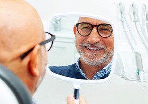 A man smiling in a mirror at his dental implants