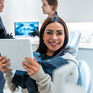 Patient smiling while holding mirror in treatment chair