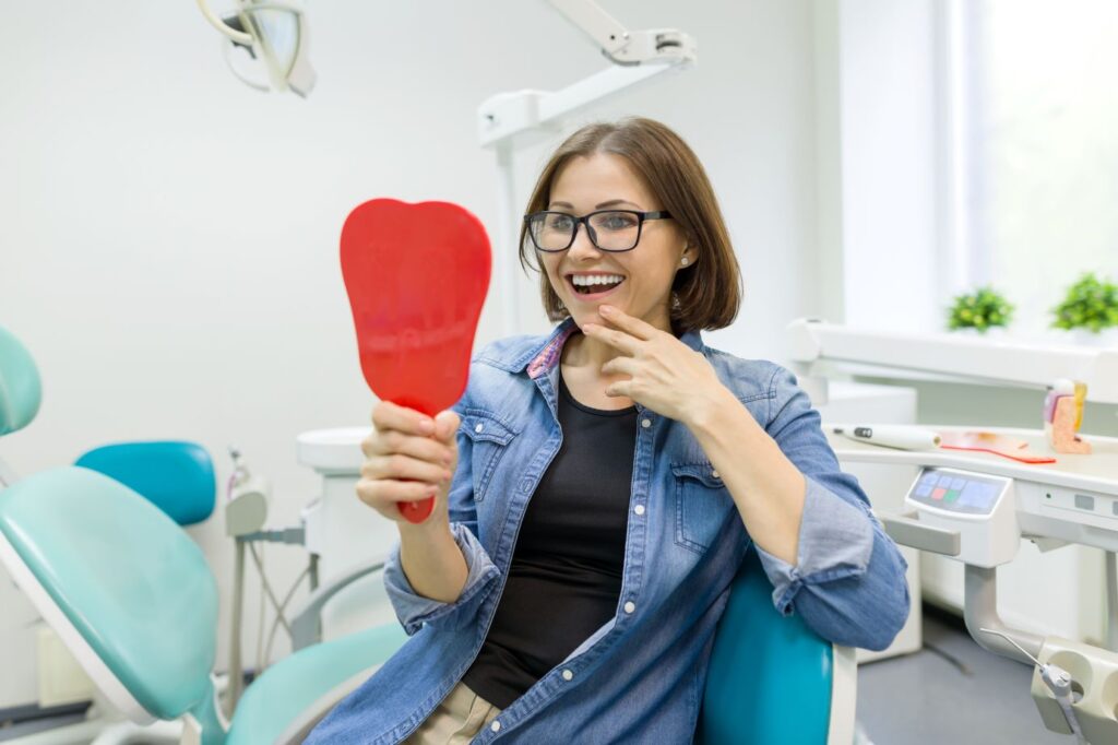 A woman at the dentist’s office looking in a mirror at her smile